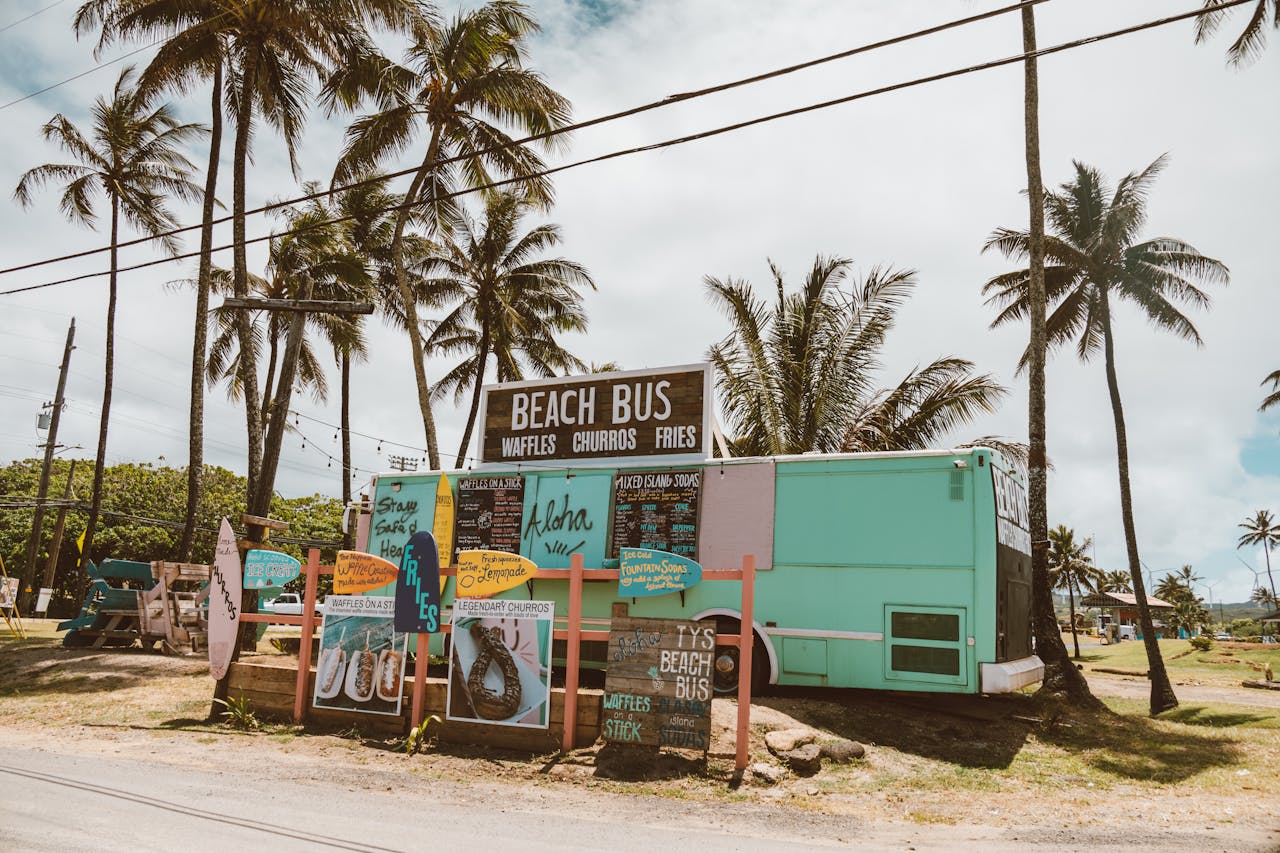 Beach bus food truck in Hawaii offering waffles, churros, and fries under palm trees.
